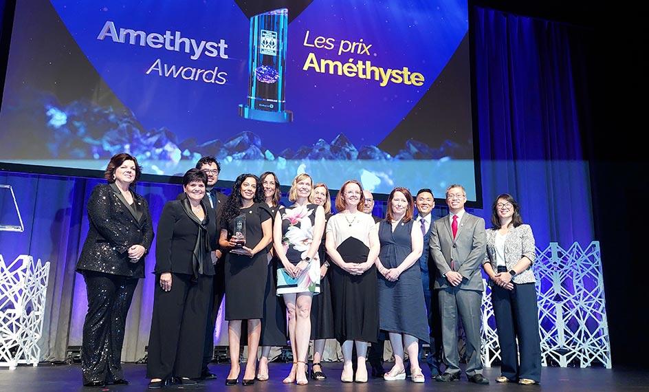 Des membres de l’équipe du programme provincial de génétique sourient sur scène avec leur trophée après avoir reçu le prix Améthyste.